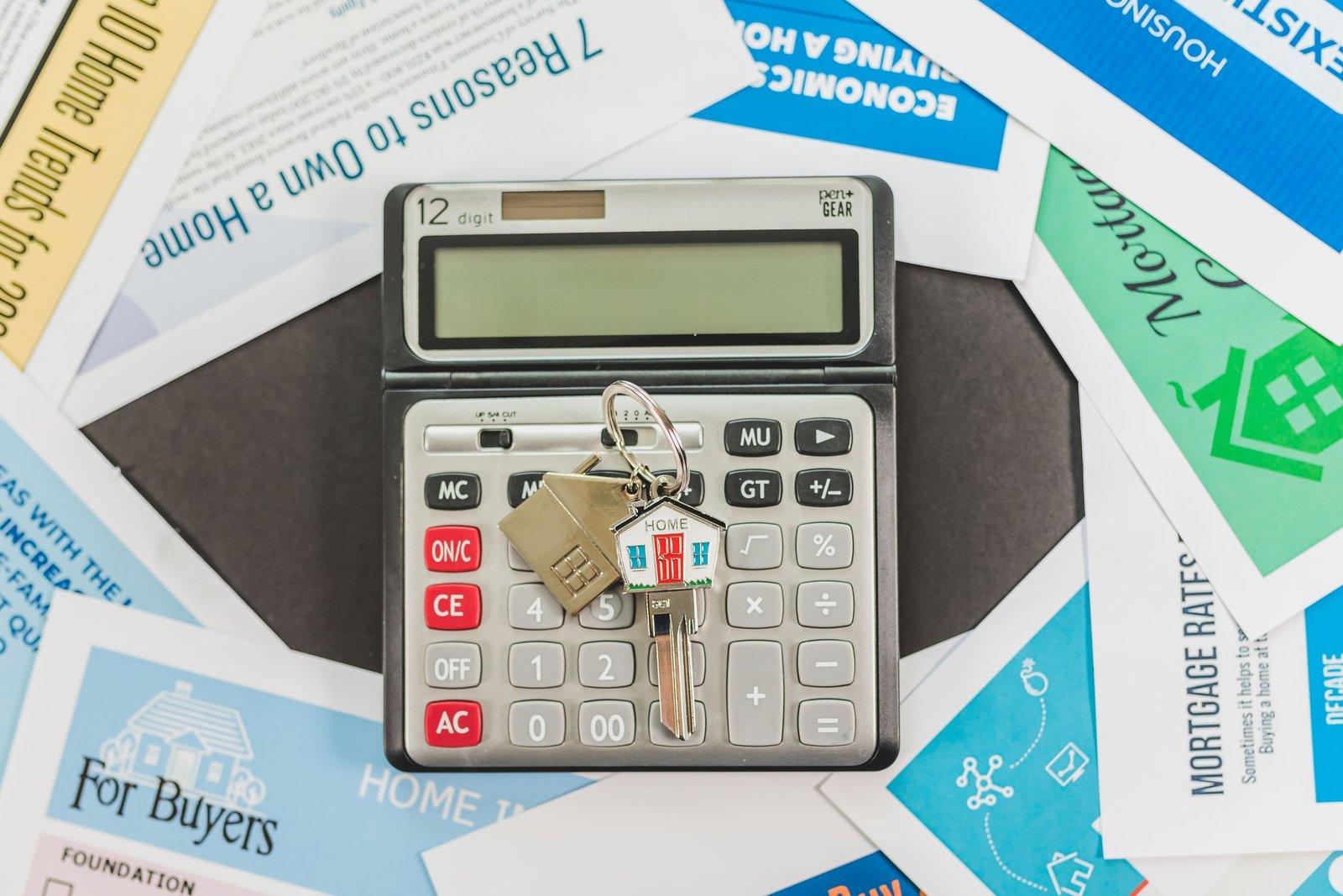 Calculator with a house-shaped key chain and house key resting on home buying flyers