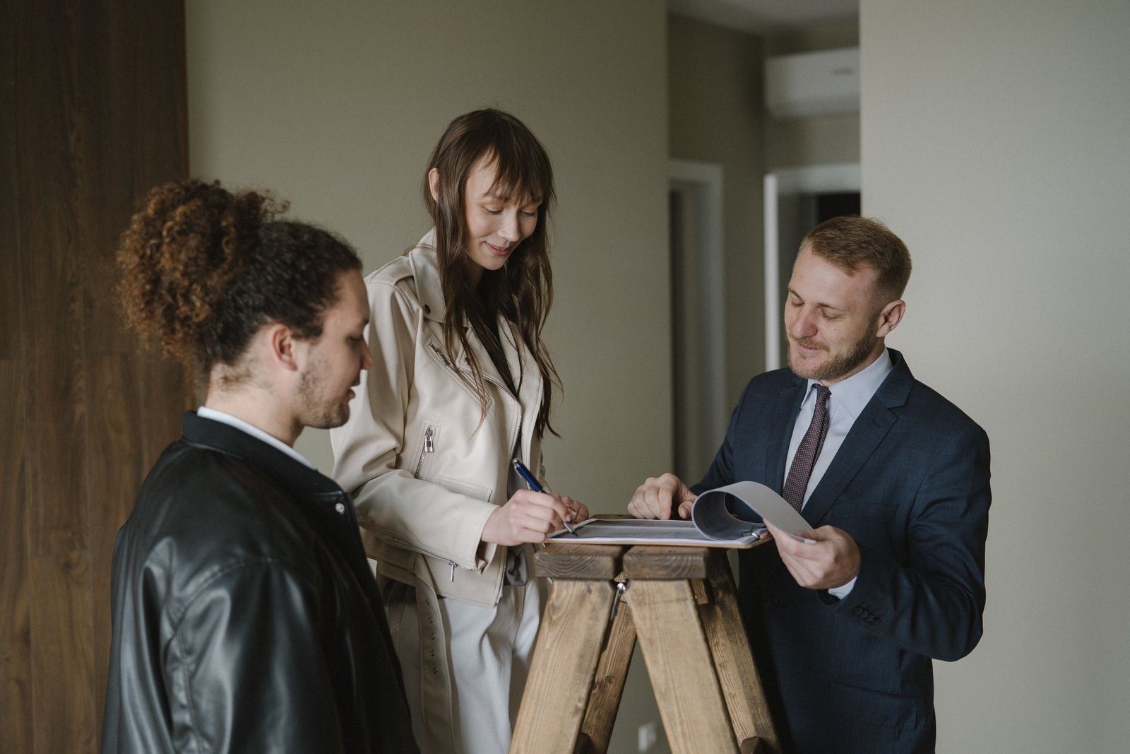 Couple reviewing and signing home purchase documents with a real estate agent inside a home