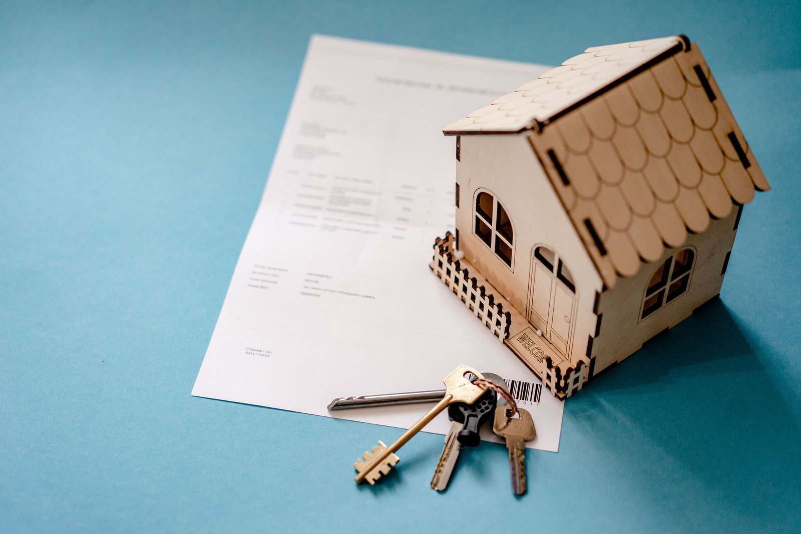 Miniature wooden house model with house keys and a signed contract on a table