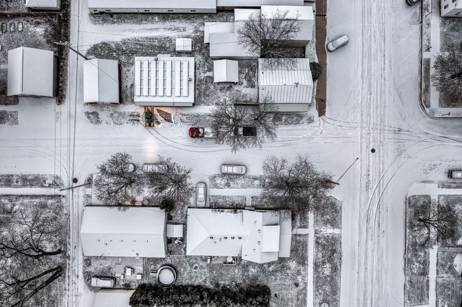 Snow-covered Midwestern suburban neighborhood with rooftops, bare trees, and tire tracks on winter streets