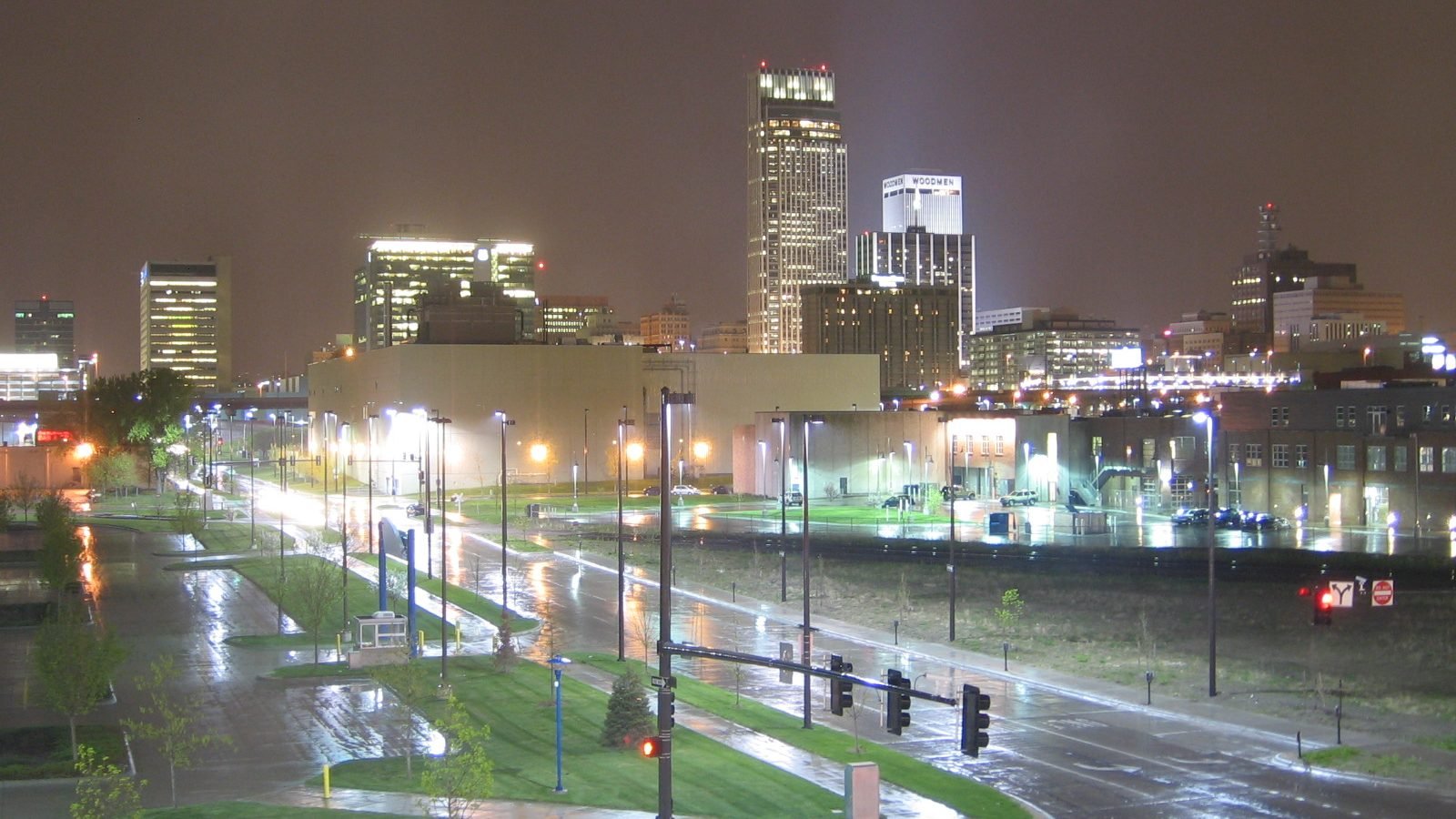 Downtown Omaha skyline at night during rainfall, with wet streets reflecting the city lights
